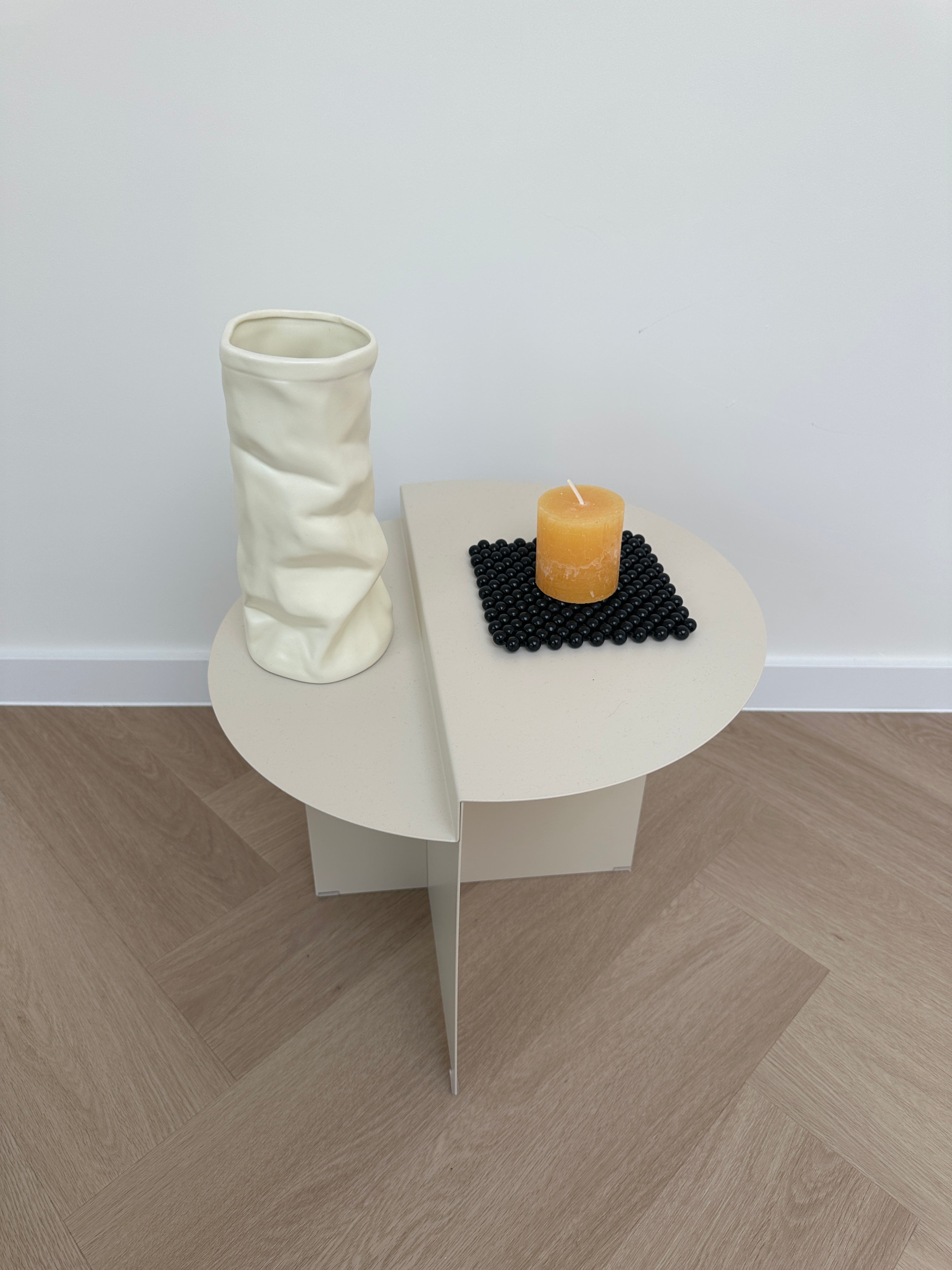 A modern wall-mounted toilet paper holder with a white oval backplate, a white paper tube holder, a black textured mat, and a small yellow holder, shown against a white wall and light wood herringbone floor.