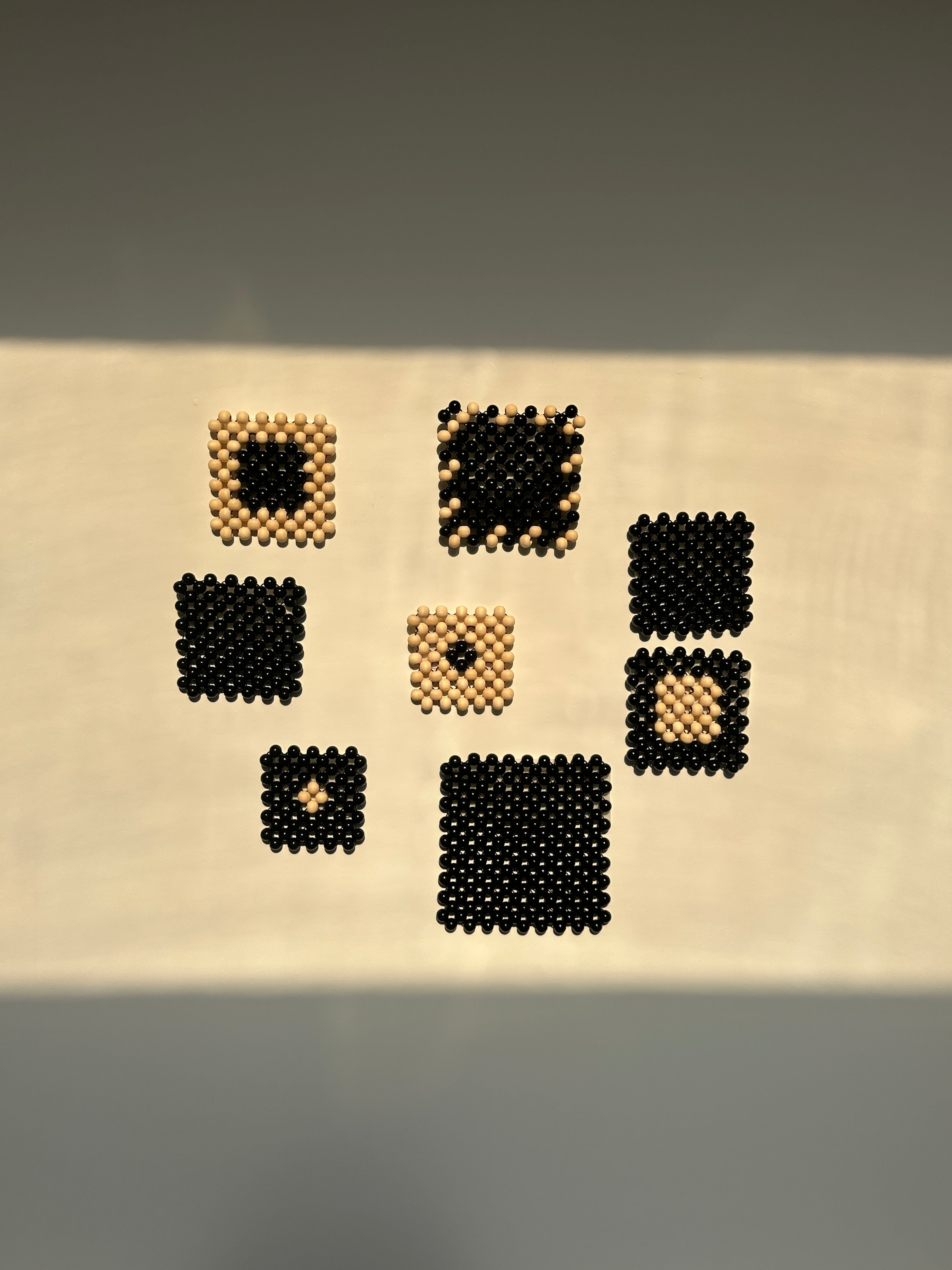 A vertical cream fabric panel with multiple small square woven or embroidered motifs in black and beige, photographed against a soft gray background.